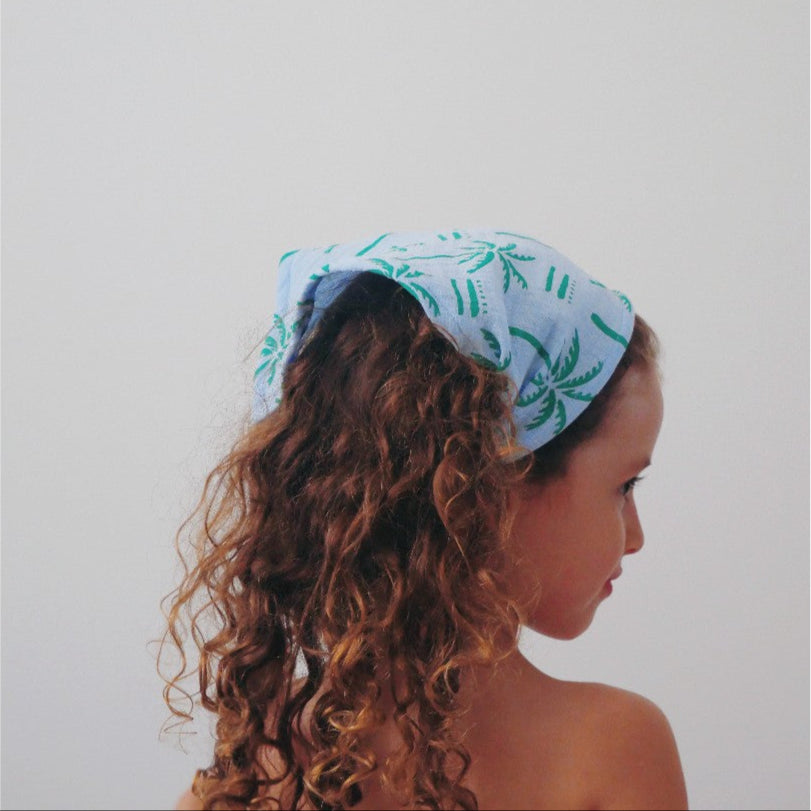 Kid wearing a light blue headscarf with green patterns on a plain background