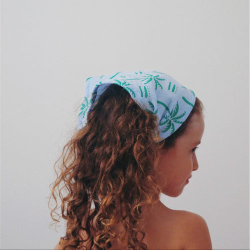 Kid wearing a light blue headscarf with green patterns on a plain background